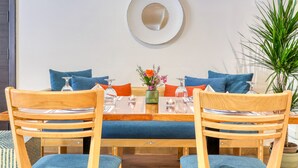 A dining area with a round table, blue upholstered chairs, and a decorative mirror on the wall. - Liwan Hotel (Amman)