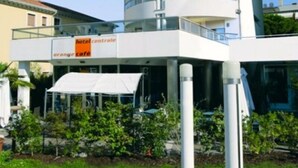 Un moderno edificio de hotel con varios balcones y una cafetería llamada "Orange Cafe" en la planta baja.