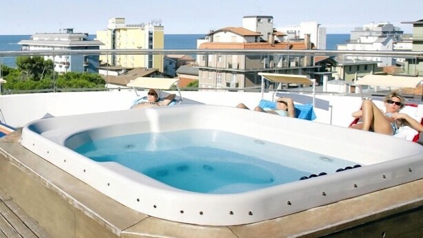 Una piscina en la azotea con un jacuzzi rodeado de sillones de descanso, con vistas a una ciudad costera.
