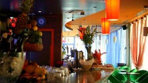 Zona de bar con exhibición de frutas, un reloj y sillas verdes.