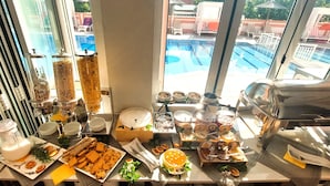 A breakfast buffet with various food items and a view of a swimming pool.