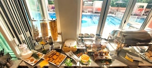A breakfast buffet with various food items and a view of a swimming pool. - Angelina Hotel & Apartments (Corfu)