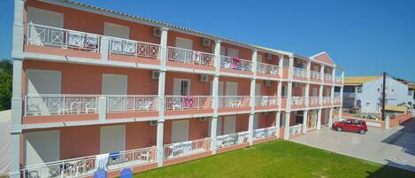 A multi-story hotel with balconies, a parking area, and a grassy lawn.