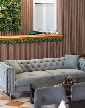 A modern living room with a tufted grey sofa, a wooden coffee table, and a small decorative plant on a shelf. - Angelina Hotel & Apartments (Corfu)