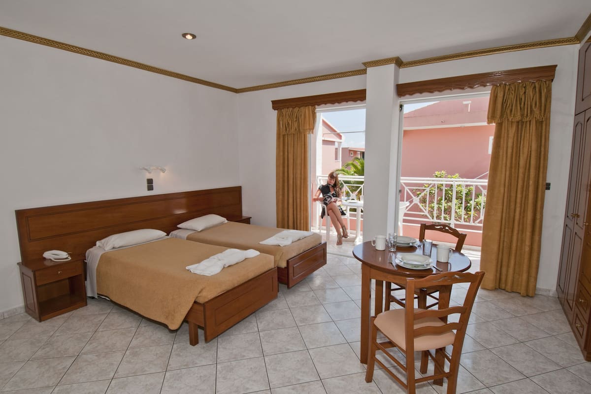 Een hotelkamer met twee bedden, een eettafel en een balkon met uitzicht.