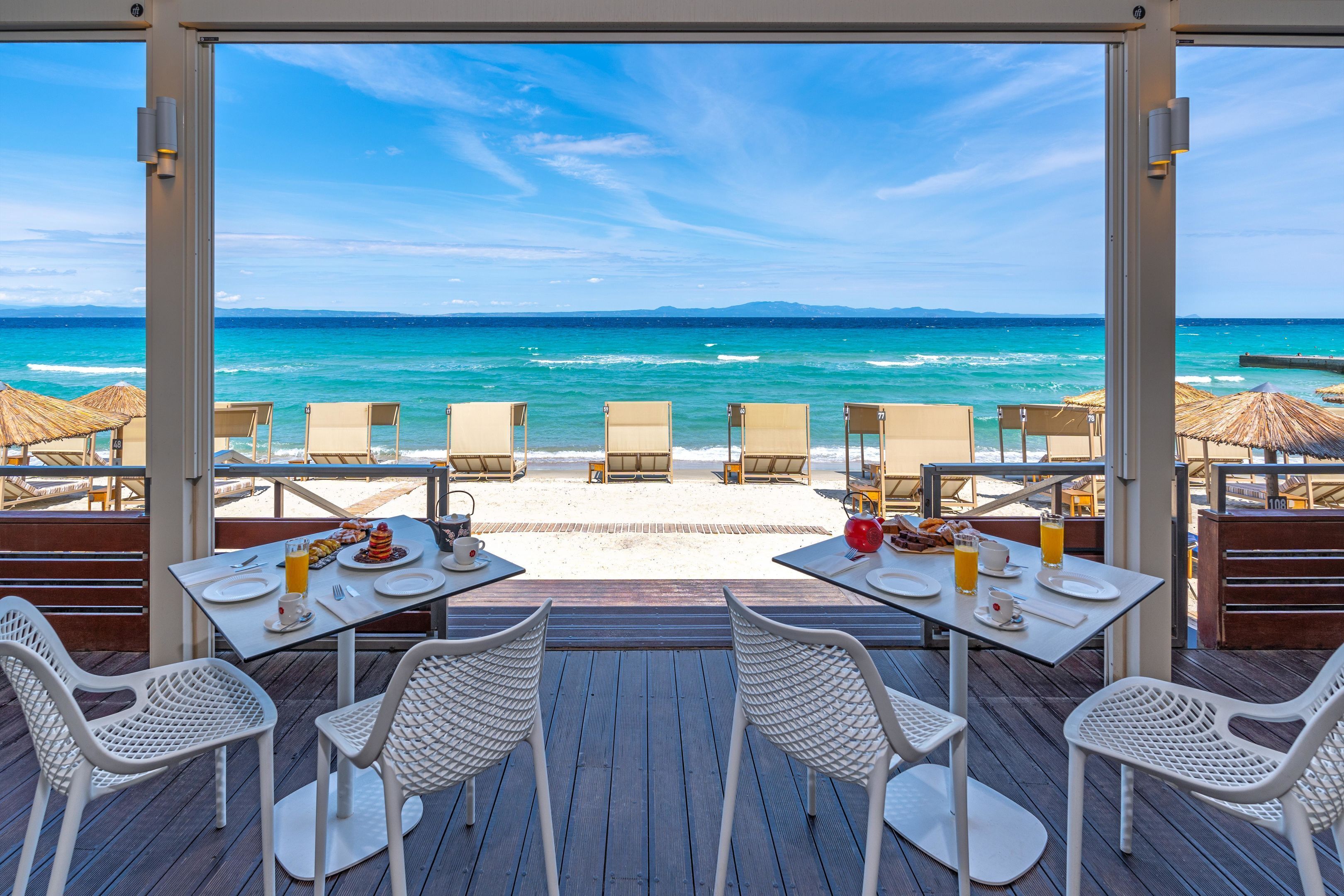 Un restaurant situé en bord de mer, avec des tables et des chaises disposées face à l’océan.