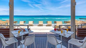 Un restaurant situé en bord de mer, avec des tables et des chaises disposées face à l’océan.