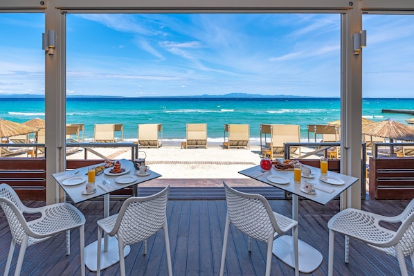 A beachside restaurant with tables and chairs facing the ocean. - Ammon Zeus Luxury Beach Hotel (Kassandra)