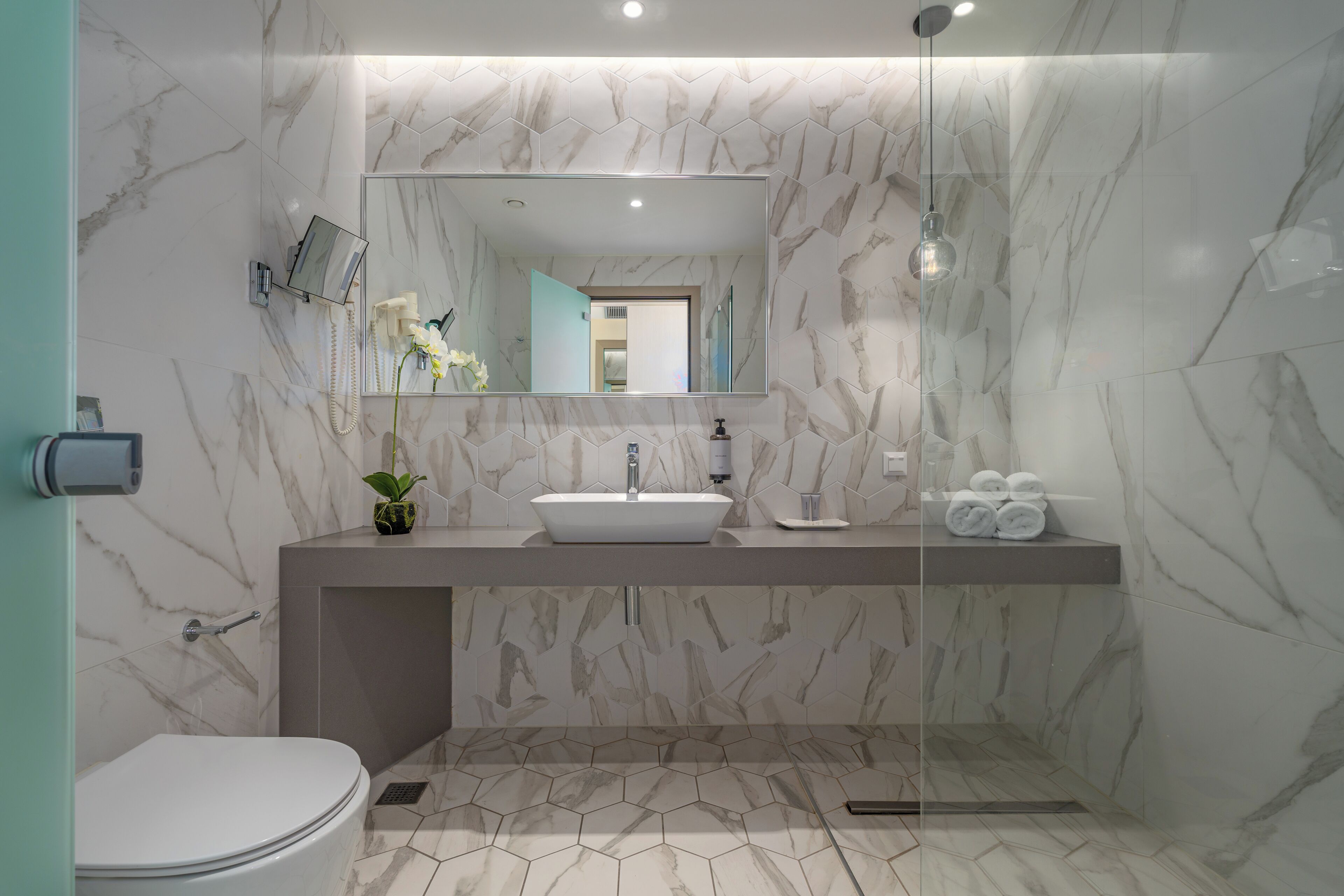 A modern bathroom with a white toilet, a large mirror, a sink, and a shower area.