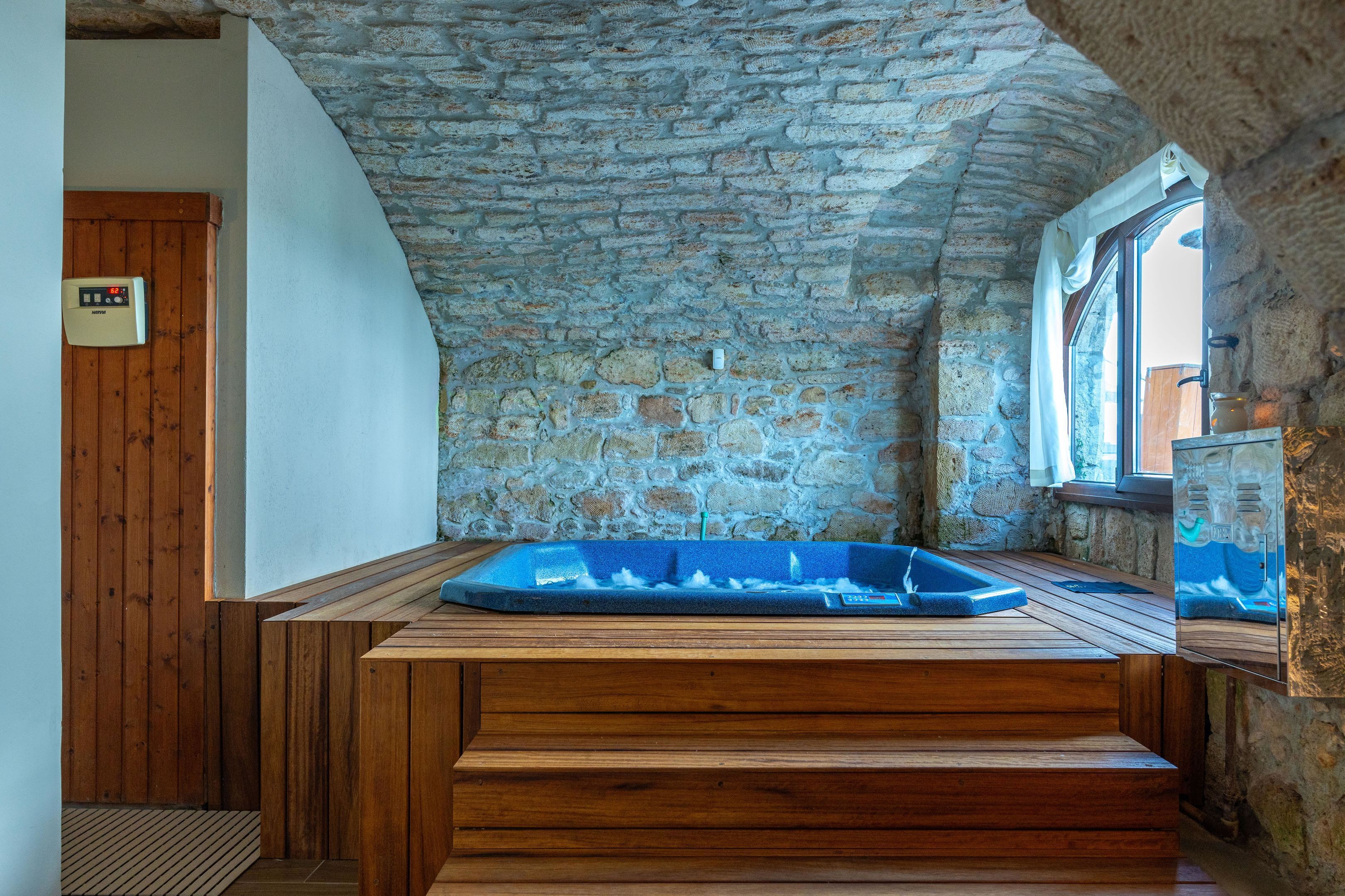 A stone-walled room with a wooden bench and a blue bathtub.