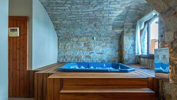 A stone-walled room with a wooden bench and a blue bathtub.