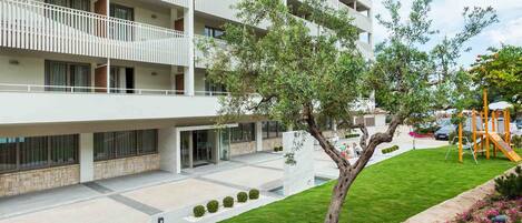 A multi-story hotel with balconies, a playground, and a well-maintained lawn.