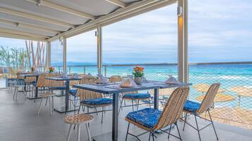 An outdoor dining area with tables and chairs, overlooking a beach and the sea.