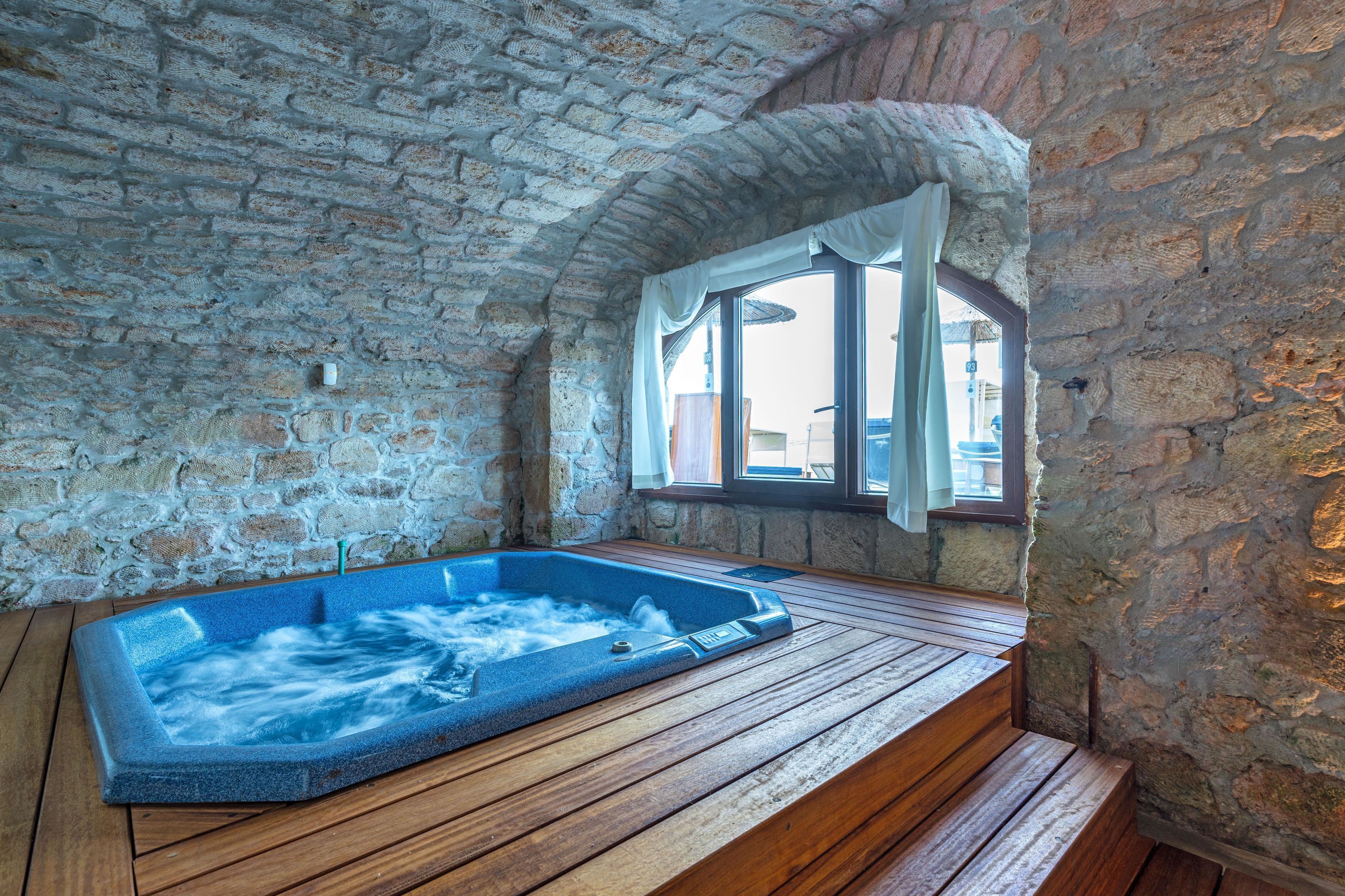 A stone-walled room with a wooden bench and a hot tub.