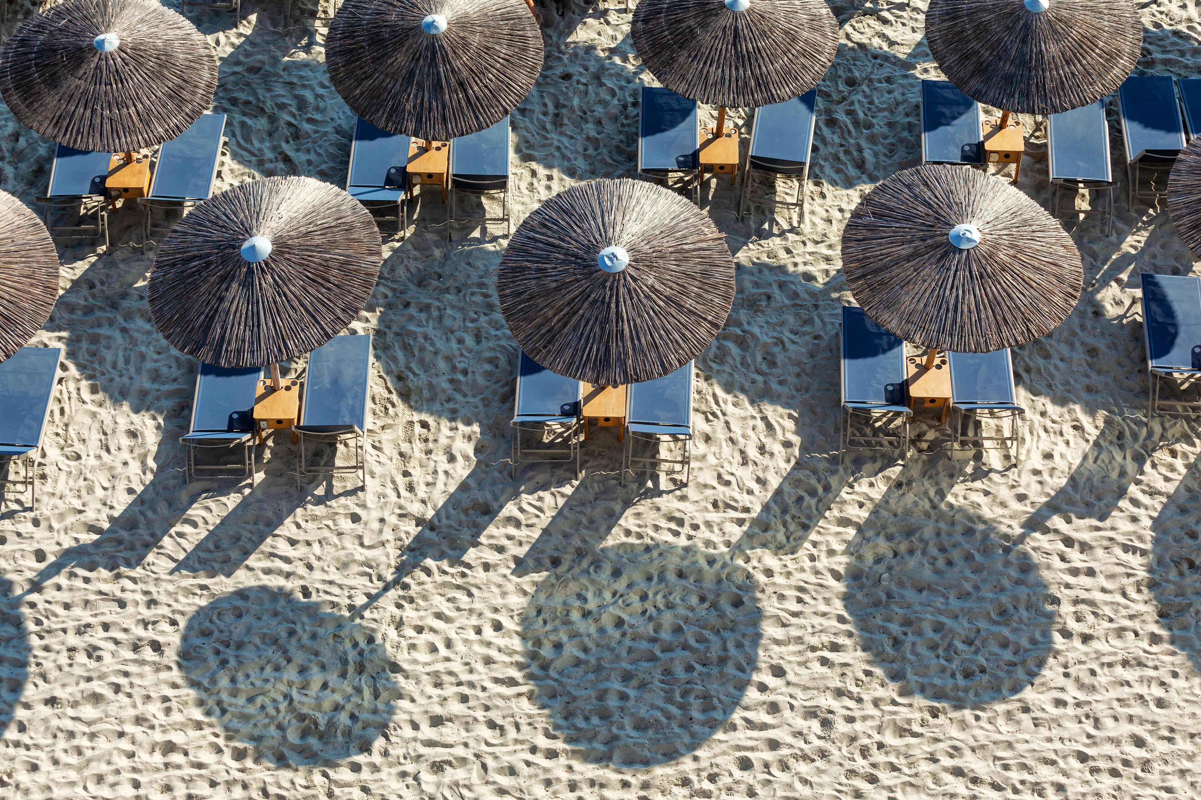 An aerial view of a beach with multiple sun umbrellas and lounge chairs arranged in rows.