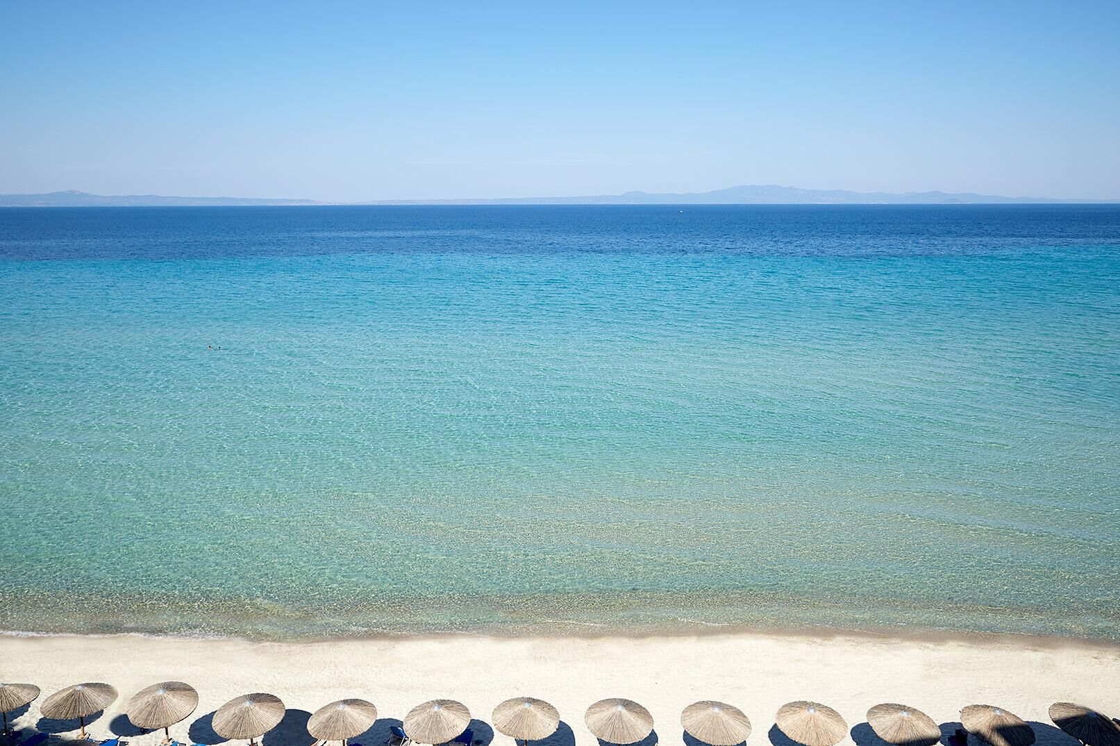 Una playa con agua turquesa cristalina y una fila de sombrillas a lo largo de la orilla.