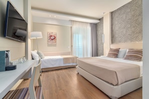 A modern hotel room with a bed, a desk, a chair, a TV, and a window with curtains.