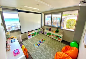 A room with a whiteboard, storage bins, a play mat, and a view of the beach.