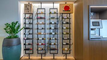 A modern hotel lobby with a wine rack displaying various bottles, a large potted plant, and a wooden wall panel.