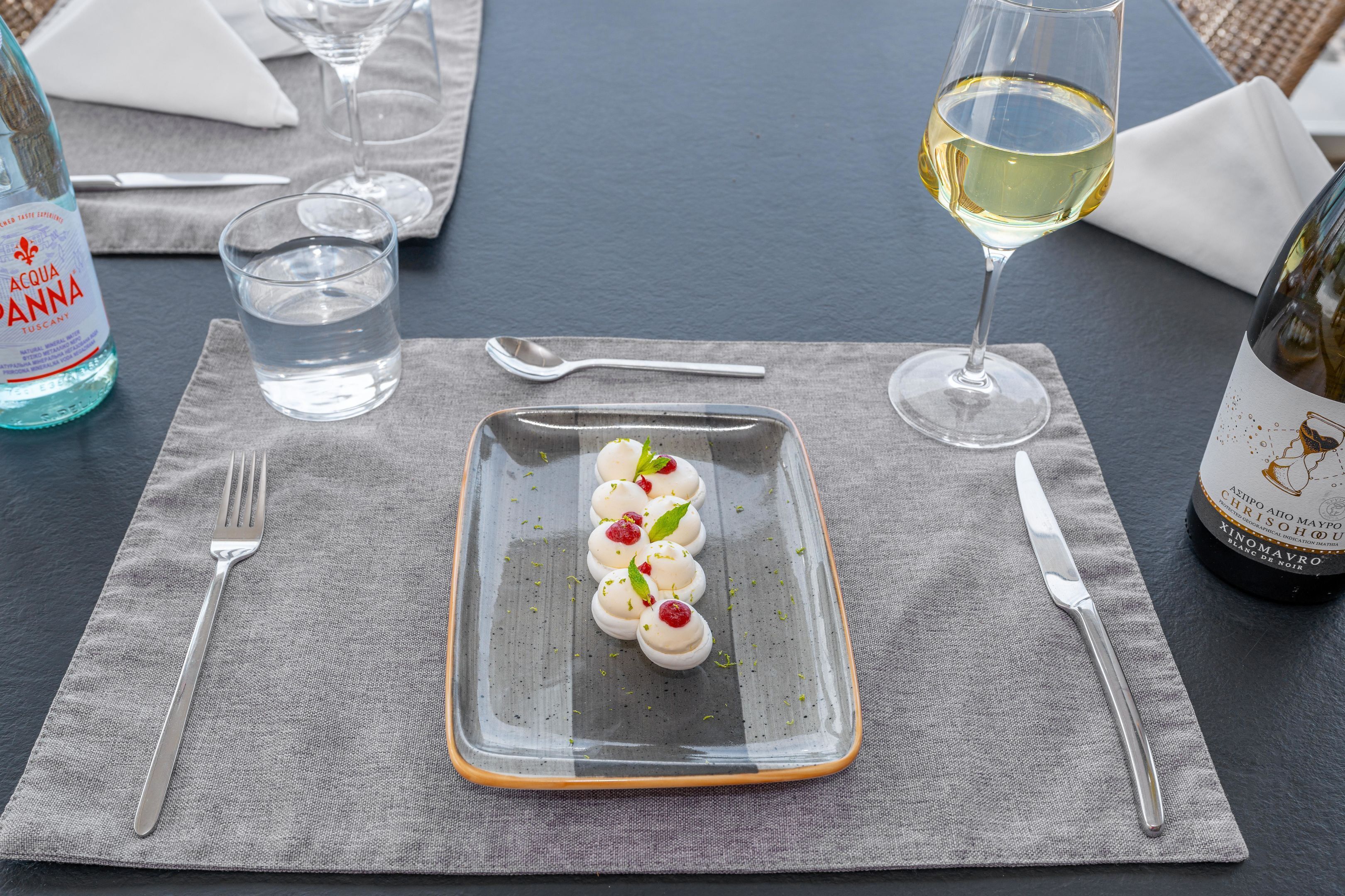 A dining table with a rectangular plate of food, a glass of water, a bottle of water, a wine glass, and a bottle of wine.