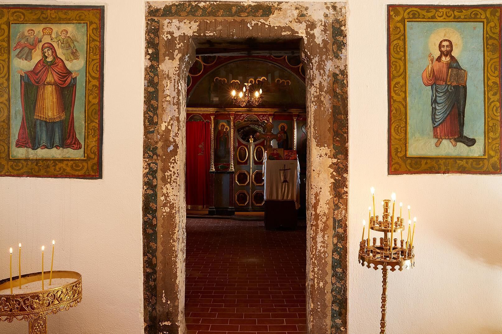 A church interior with a brick floor, a chandelier, and religious paintings on the walls.