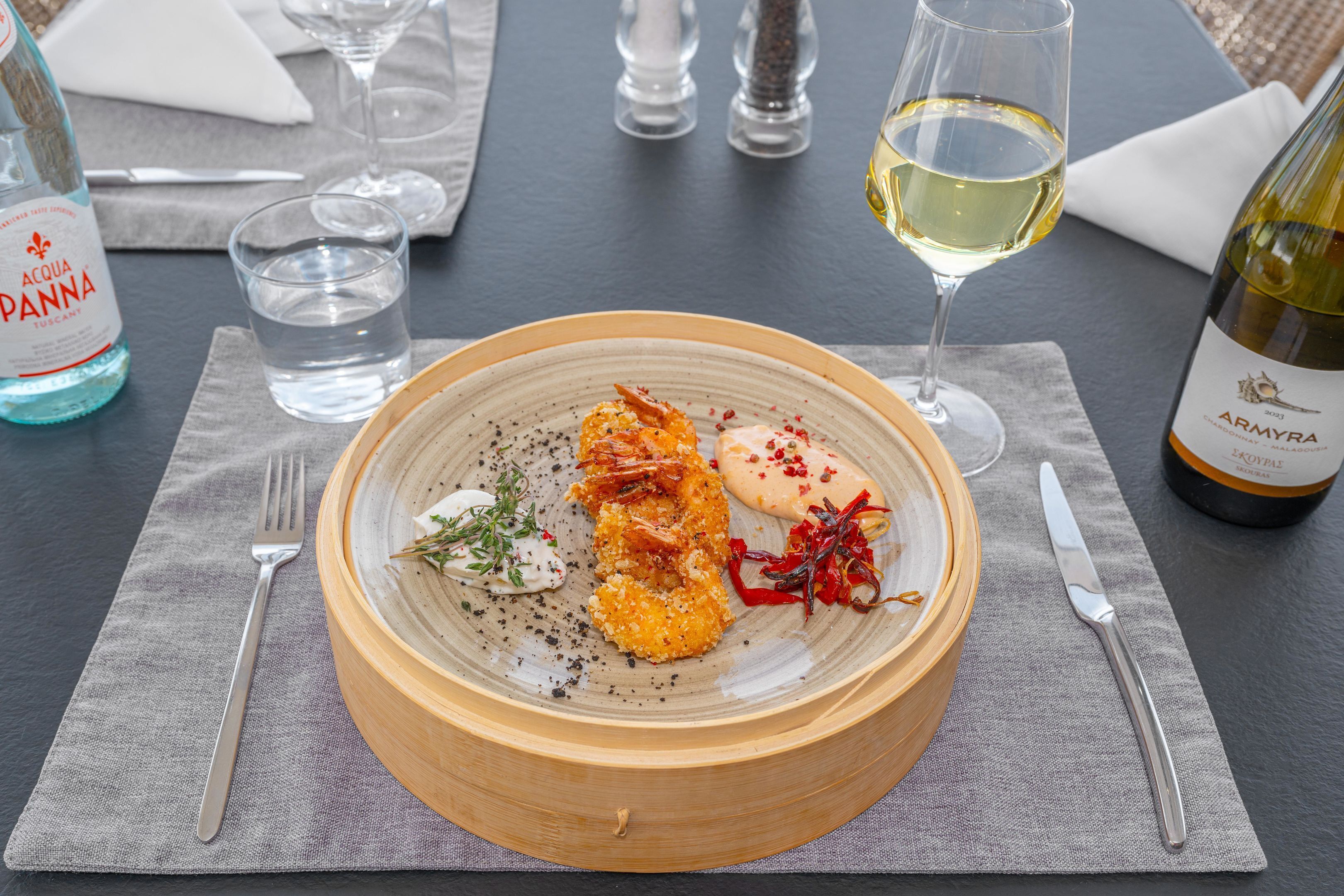 A dining table with a plate of food, a bottle of water, a glass of wine, and a bottle of olive oil.