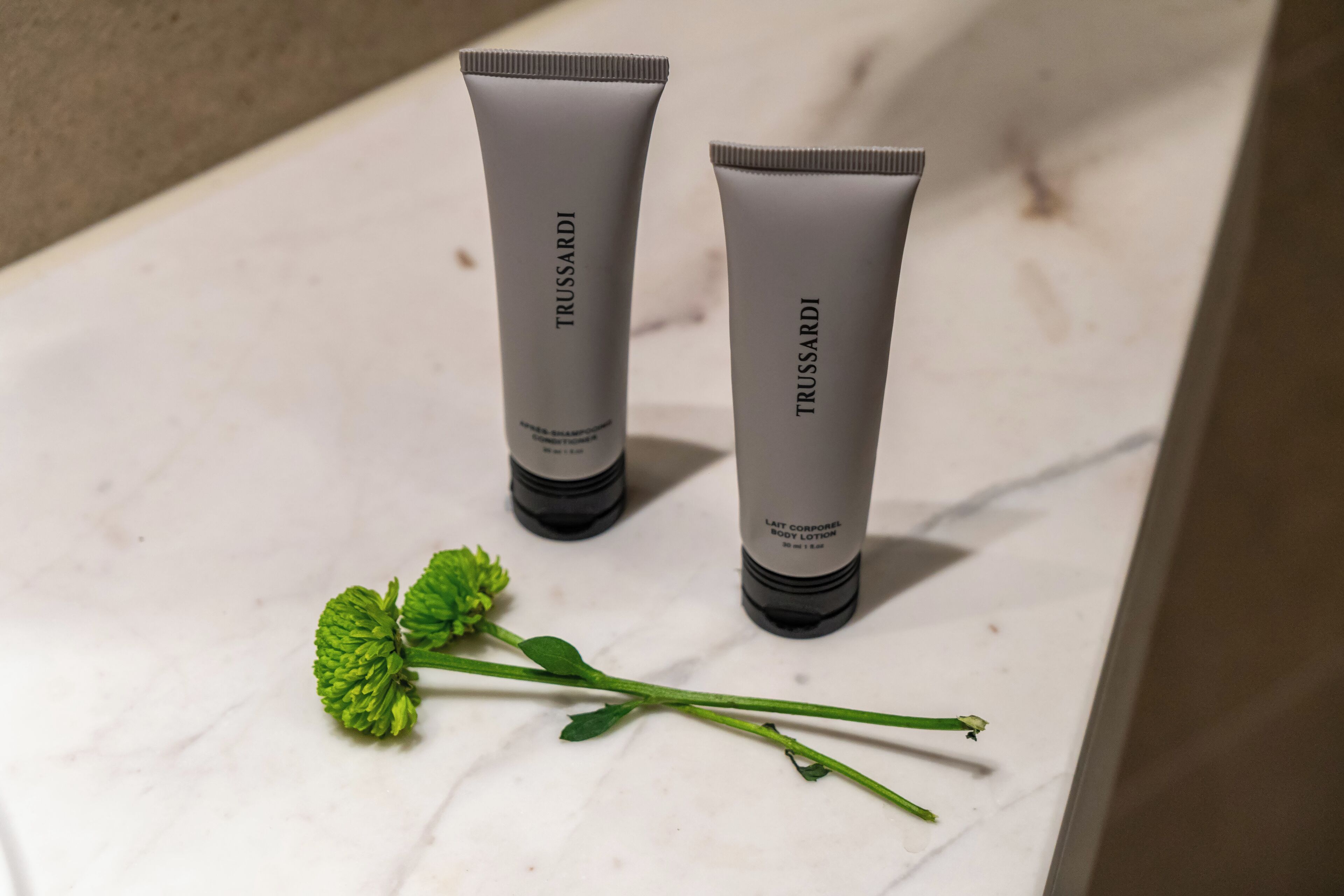 Two tubes of Trussardi body lotion on a marble surface with a green plant beside them.