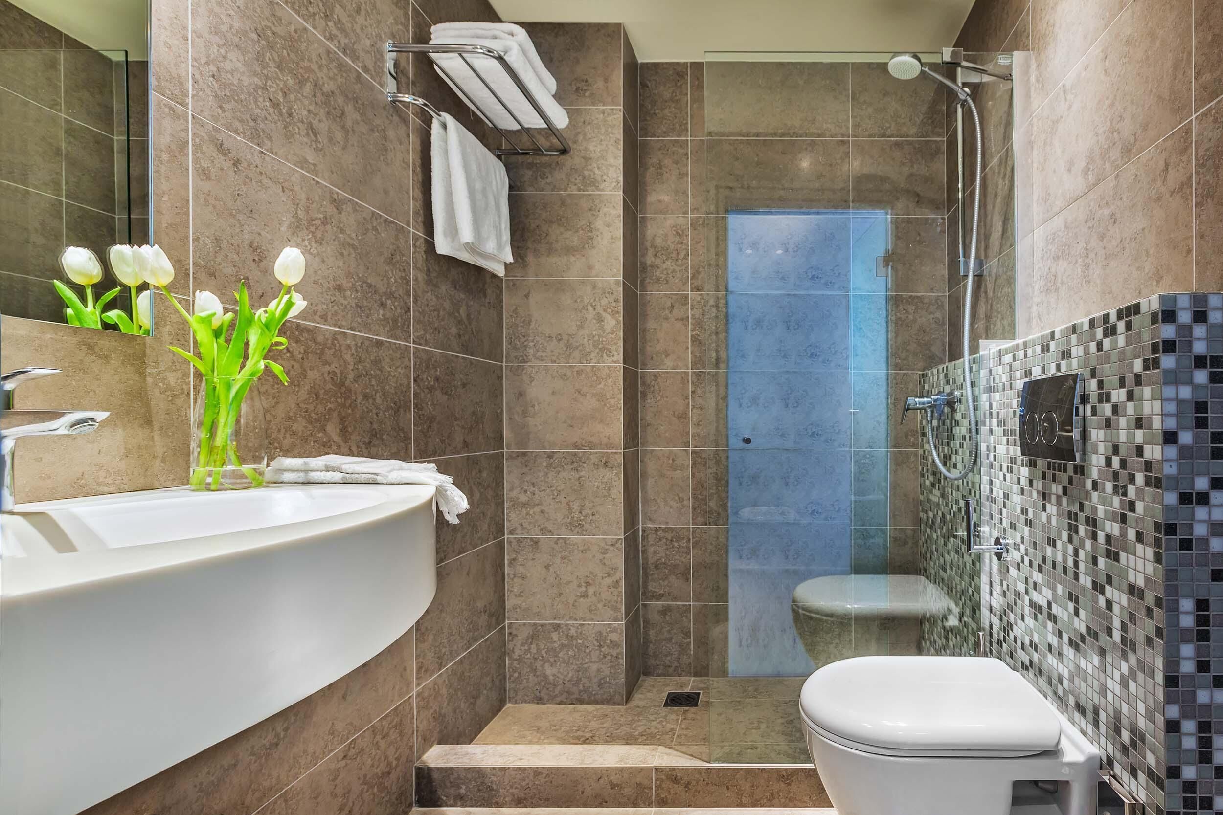 A bathroom with a white sink, a toilet, a shower with a tiled wall, and a mirror.