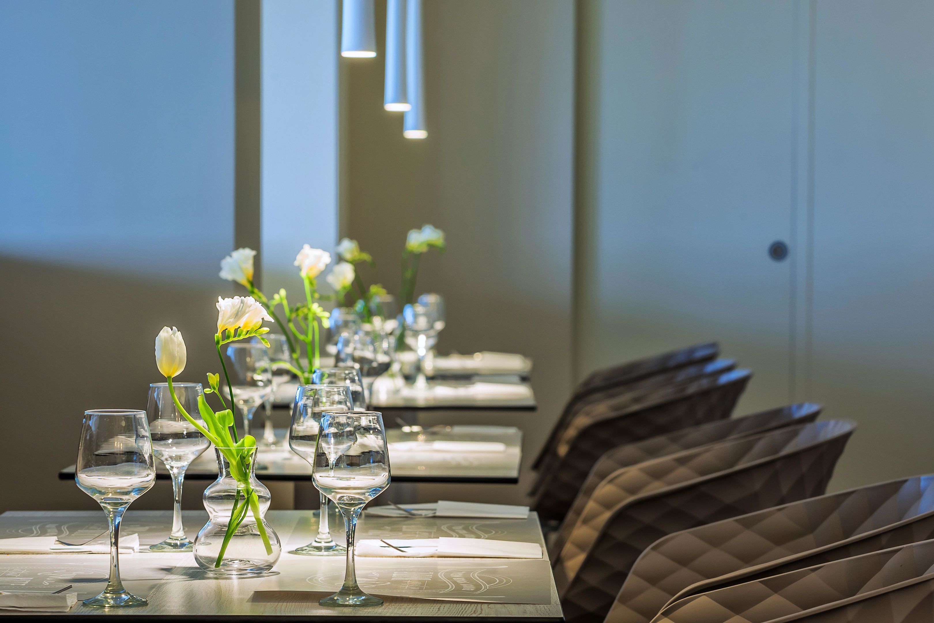 Un espace repas avec des tables dressées pour le service, agrémenté de verres transparents et de fleurs blanches dans des vases.