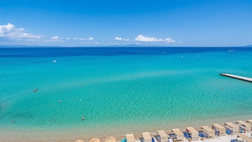 A beach with clear turquoise water, a pier, and rows of sun loungers and umbrellas.