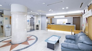 Eine Lobby mit einer Rezeption, einem Wasserspender, einer großen Säule, einer Couch und einem gemusterten Boden.