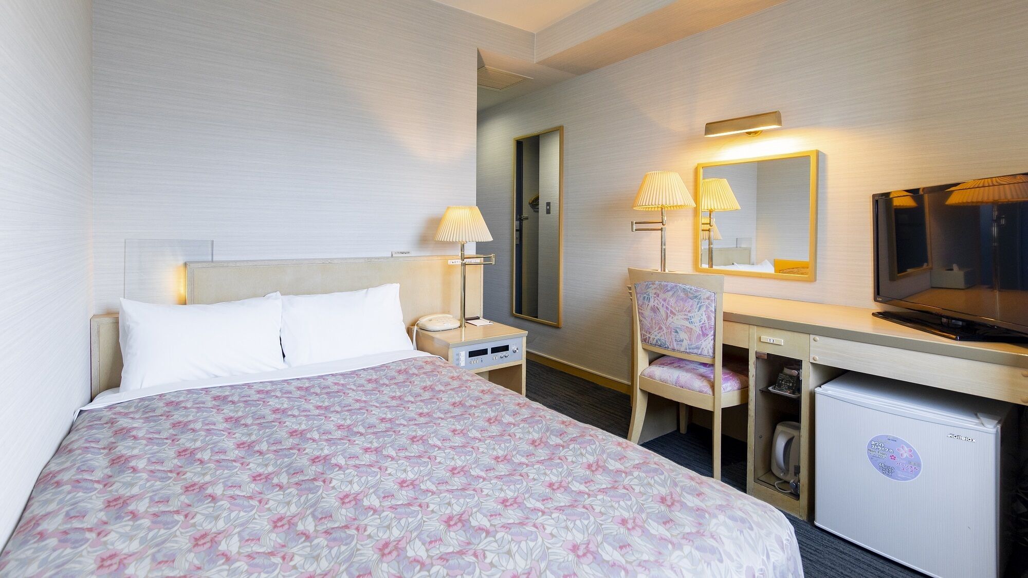 A hotel room with a bed, desk, chair, television, and a small refrigerator.