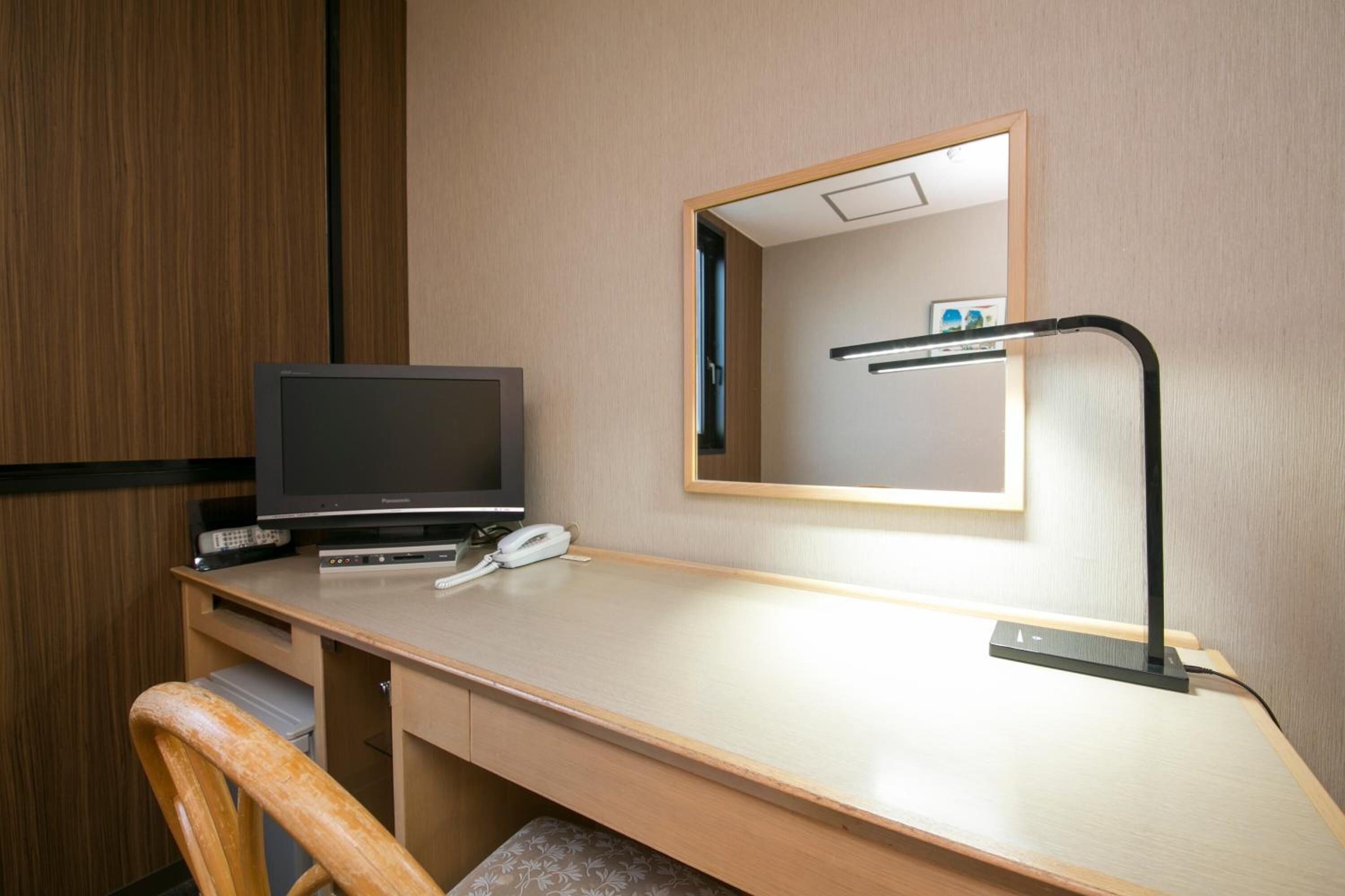 A hotel room with a wooden desk, a television, a telephone, and a mirror.