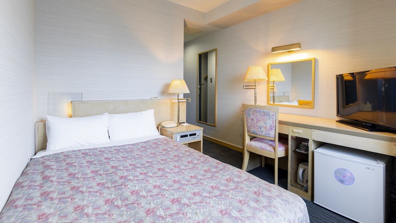 A hotel room with a bed, desk, chair, television, and a small refrigerator.