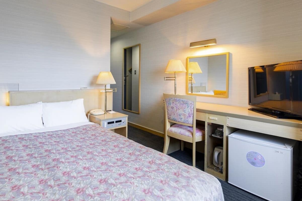 A hotel room with a bed, desk, chair, television, and a small refrigerator.