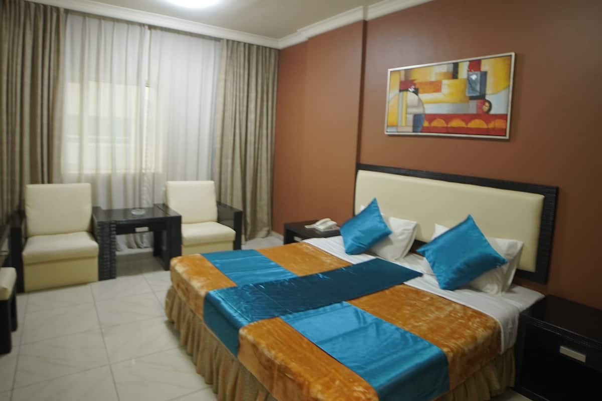 Een hotelkamer met een groot bed, twee fauteuils, een bijzettafeltje en een schilderij aan de muur.