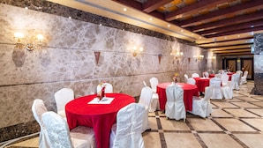 Un salón de banquetes con mesas redondas cubiertas con manteles rojos, sillas blancas y paredes de mármol.