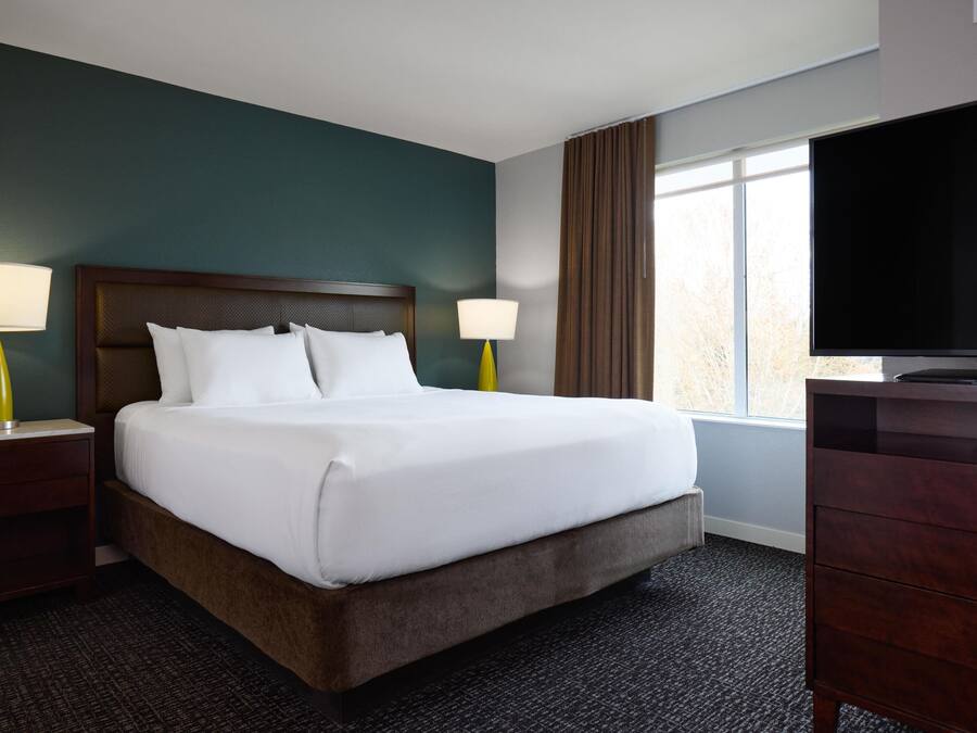 A hotel room with a large bed, two bedside tables with lamps, a dresser, and a TV.