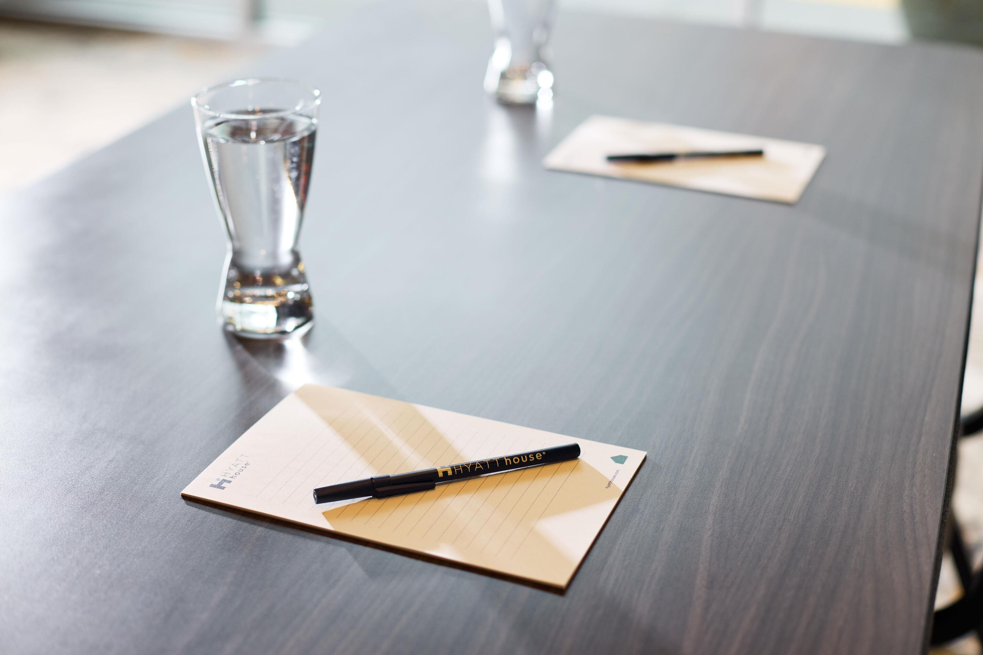 Een vergadertafel met notitieboek en pen, een glas water, en een pen op een notitieblok.