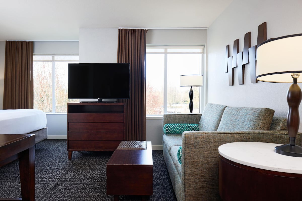 A hotel room with a bed, a TV, a sofa, a coffee table, and a lamp.