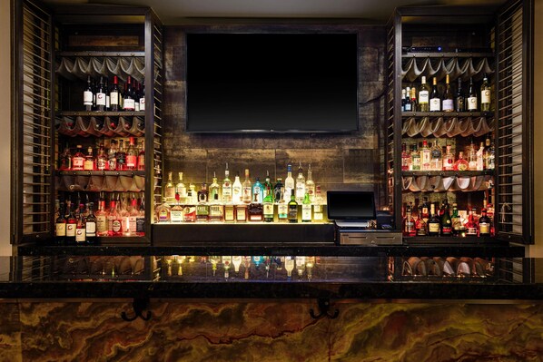 A bar area with shelves of liquor bottles, a television screen, and a marble countertop.