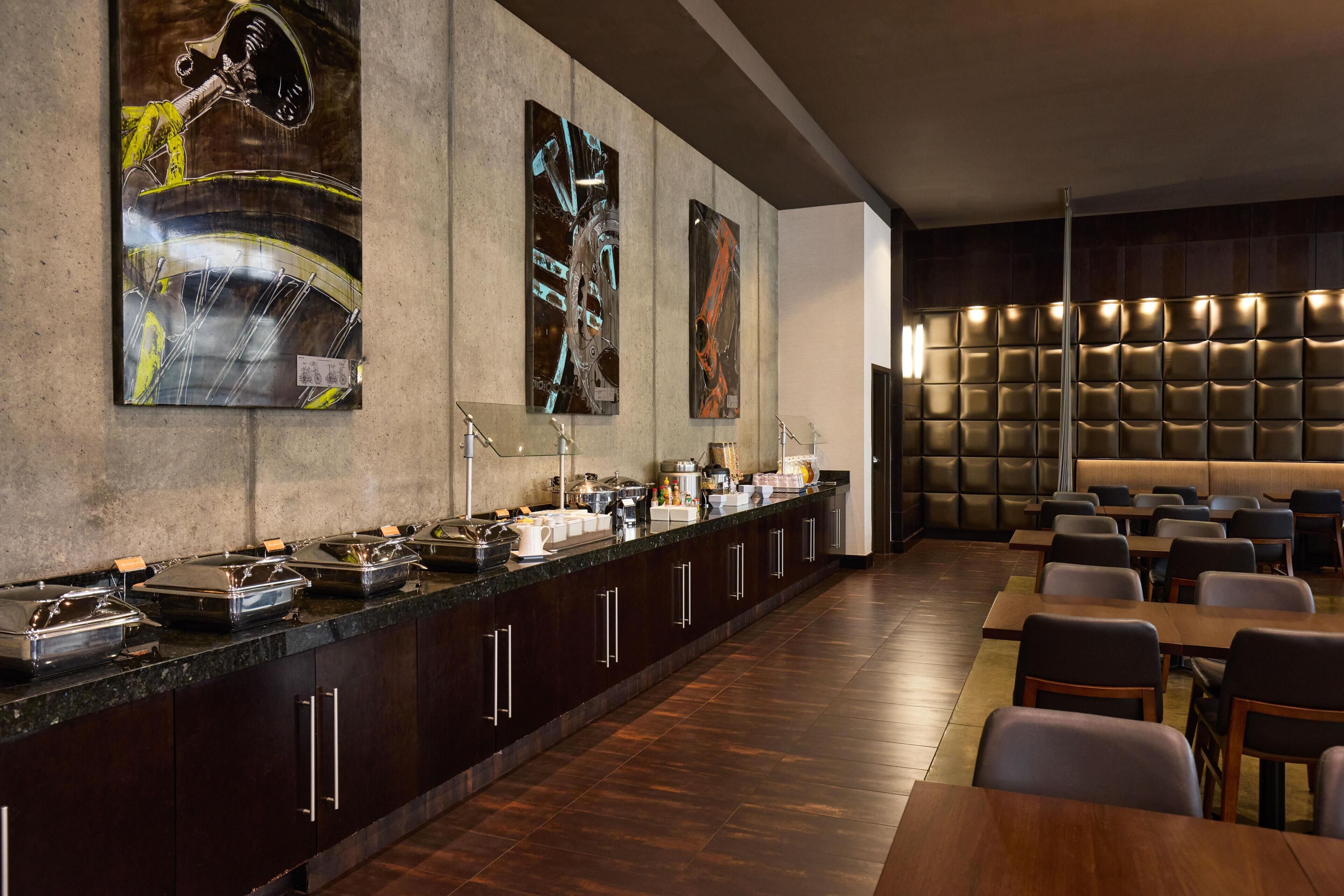 A long buffet counter with various food items and a seating area with tables and chairs.