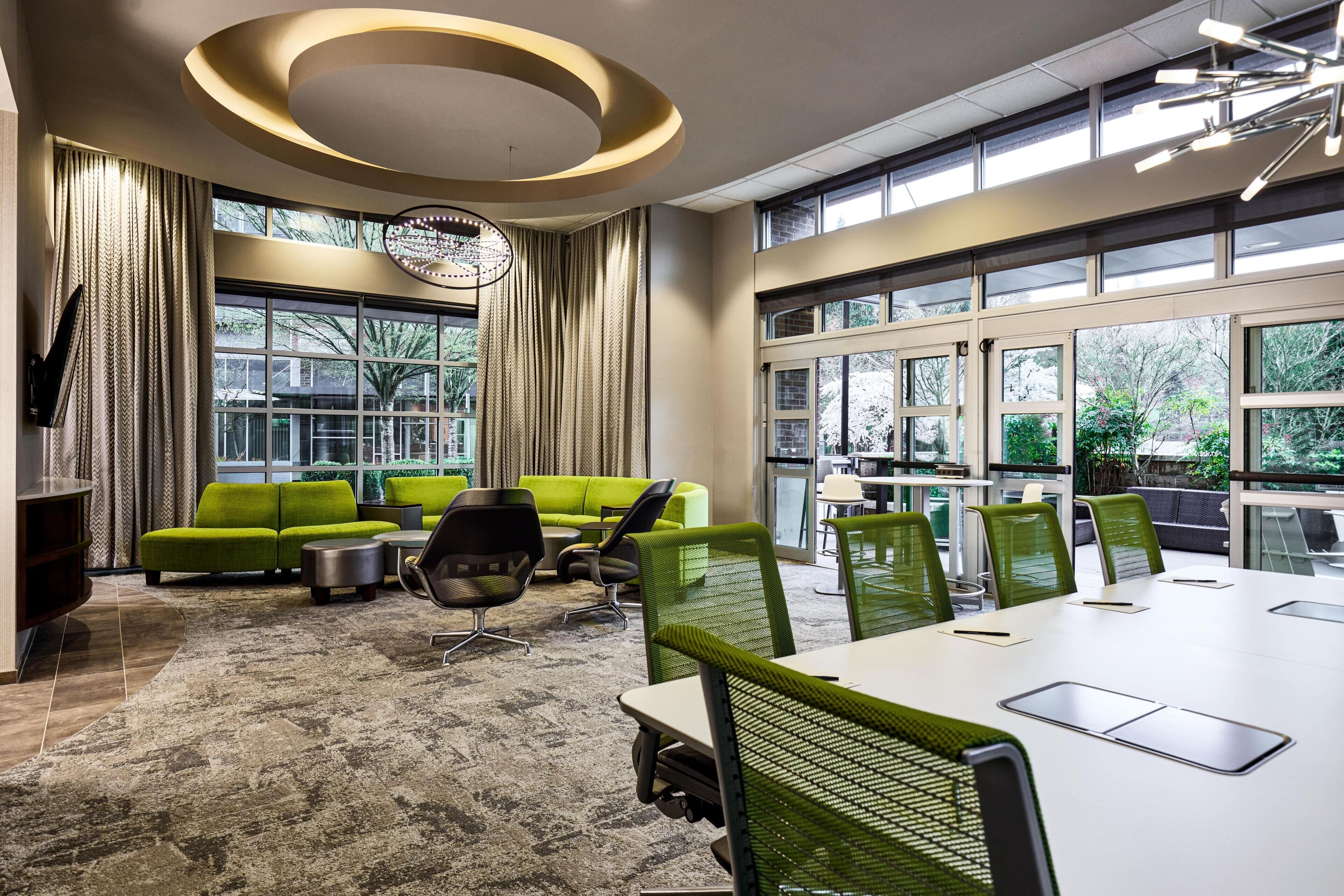 Een moderne vergaderruimte met een grote tafel, groene stoelen en een groene bank.
