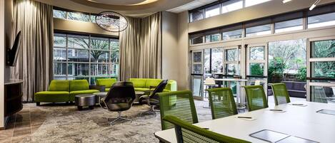 Een moderne vergaderruimte met een grote tafel, groene stoelen en een groene bank.