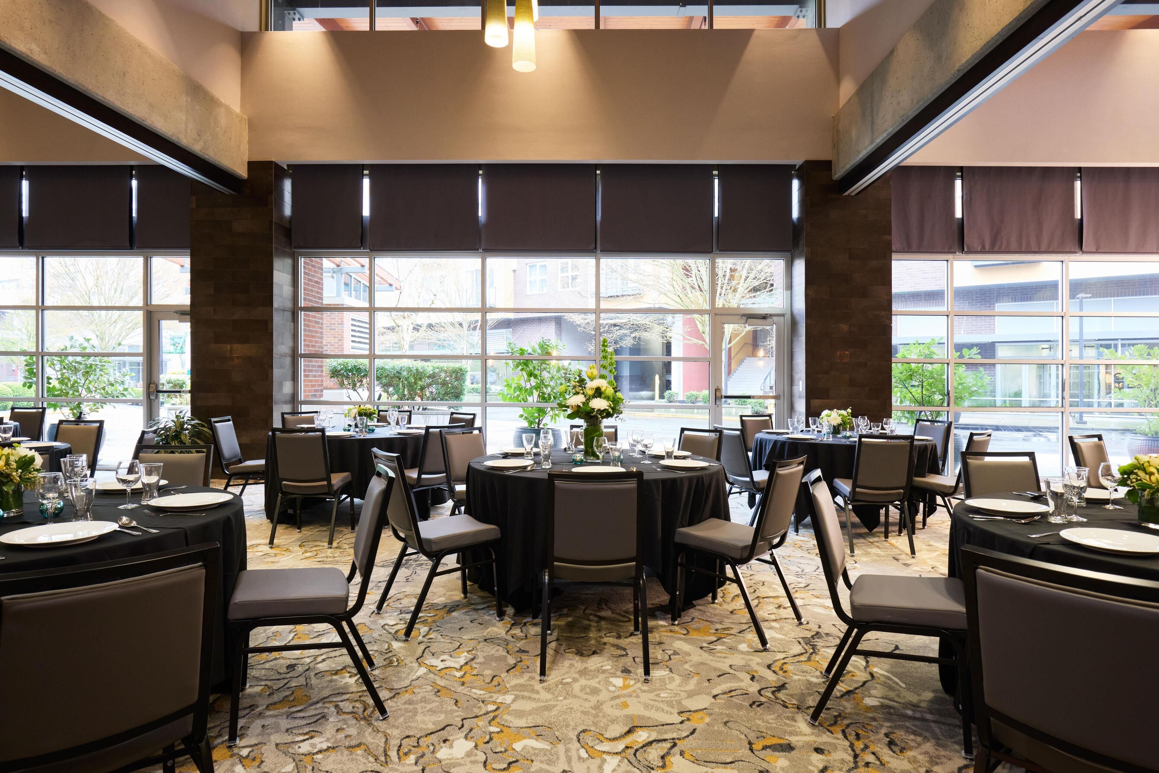 Un espace repas avec des tables rondes disposées pour accueillir six personnes, chacune agrémentée d’un vase de fleurs, d’assiettes et de couverts.