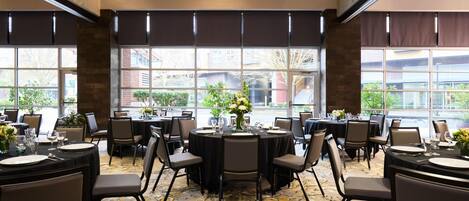 A dining area with round tables set for six, each with a vase of flowers, plates, and cutlery.