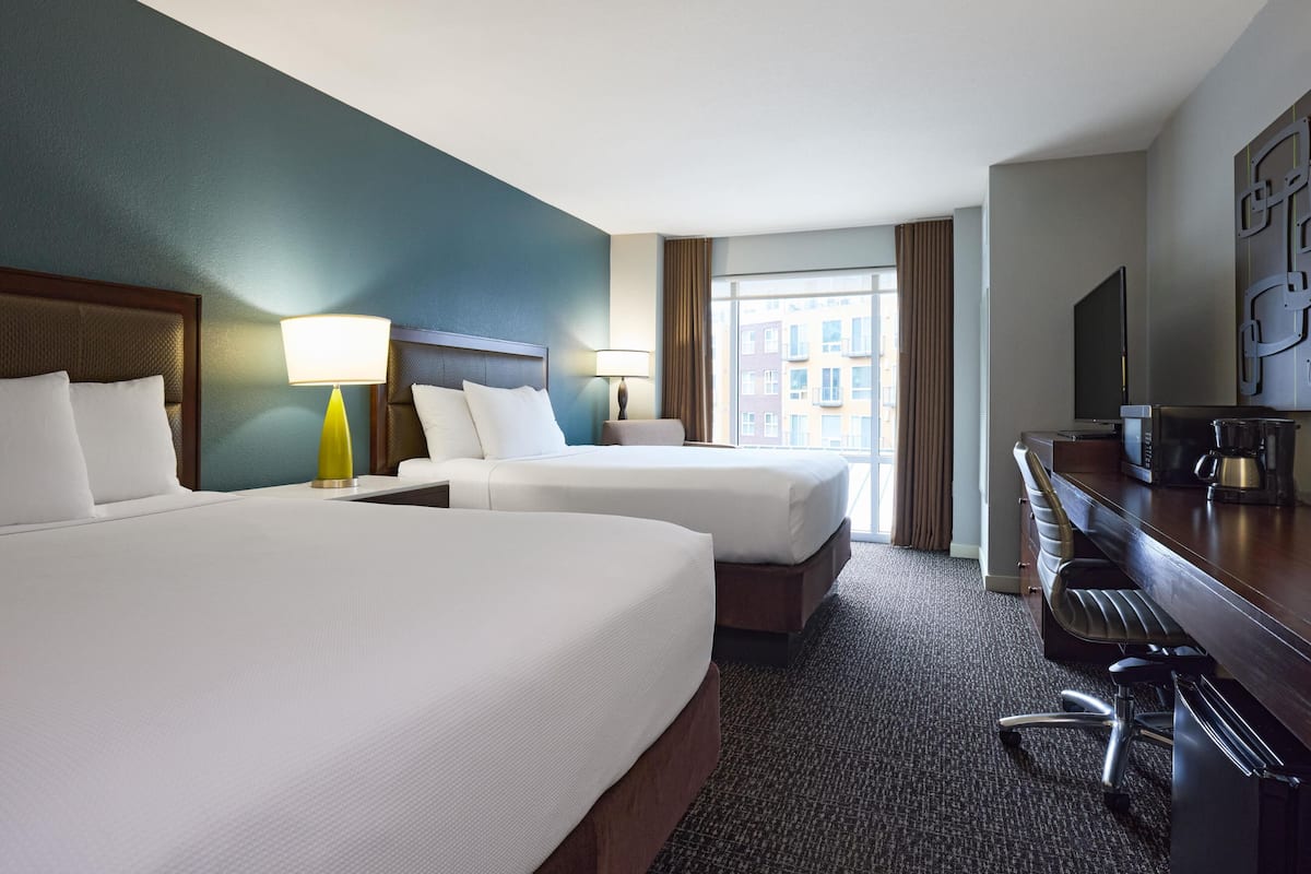 A hotel room with two beds, a desk with a chair, a TV, and a window with curtains.