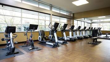 A gym with multiple cardio machines, large windows, and a wooden floor.