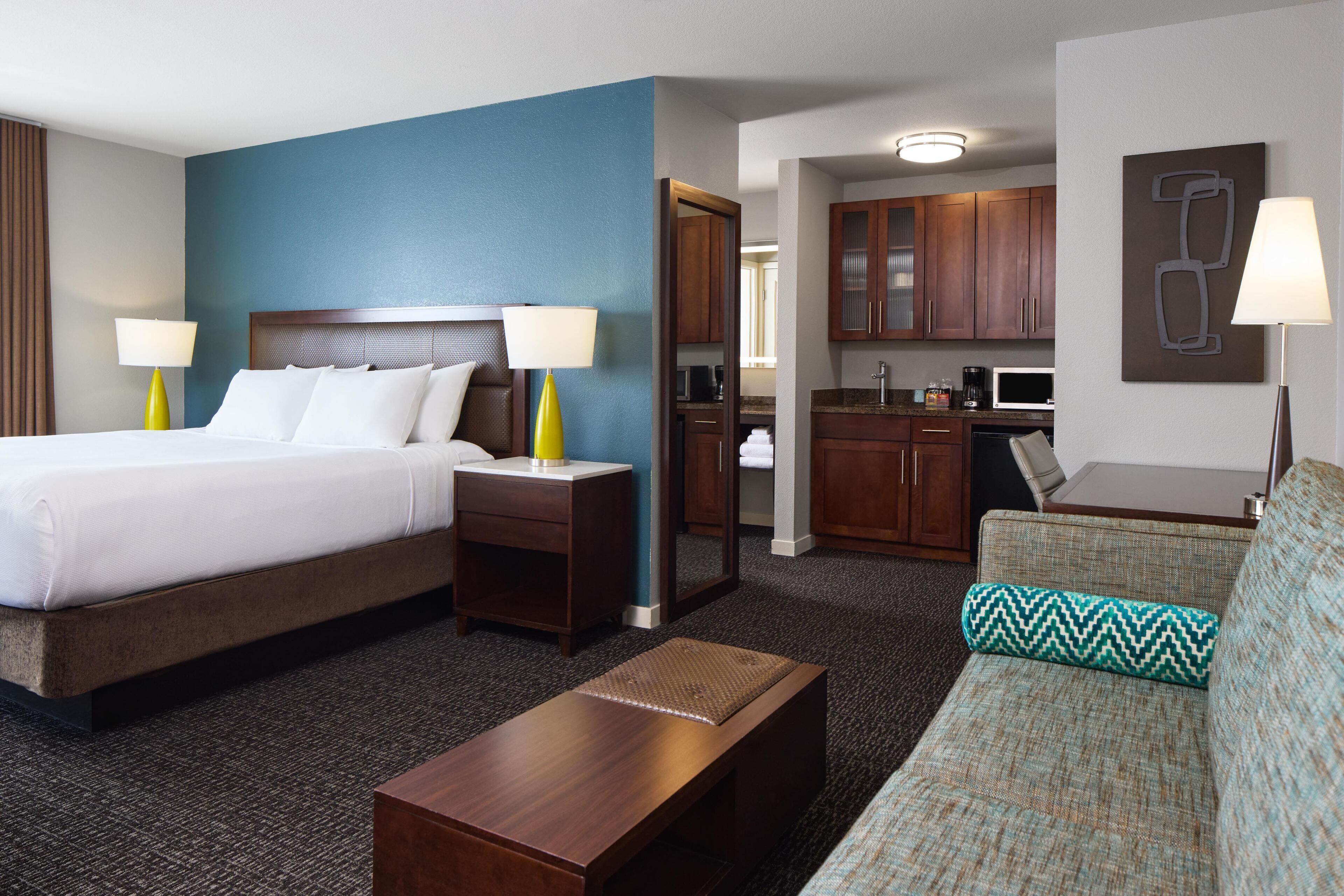 A hotel room with a bed, a sofa, a desk, and a kitchenette.
