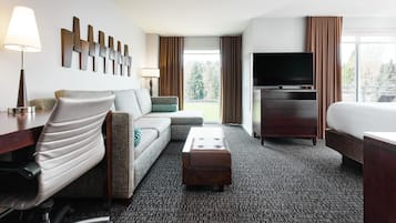 Habitación de hotel con sofá, escritorio con lámpara, televisor, cama y vista al exterior.